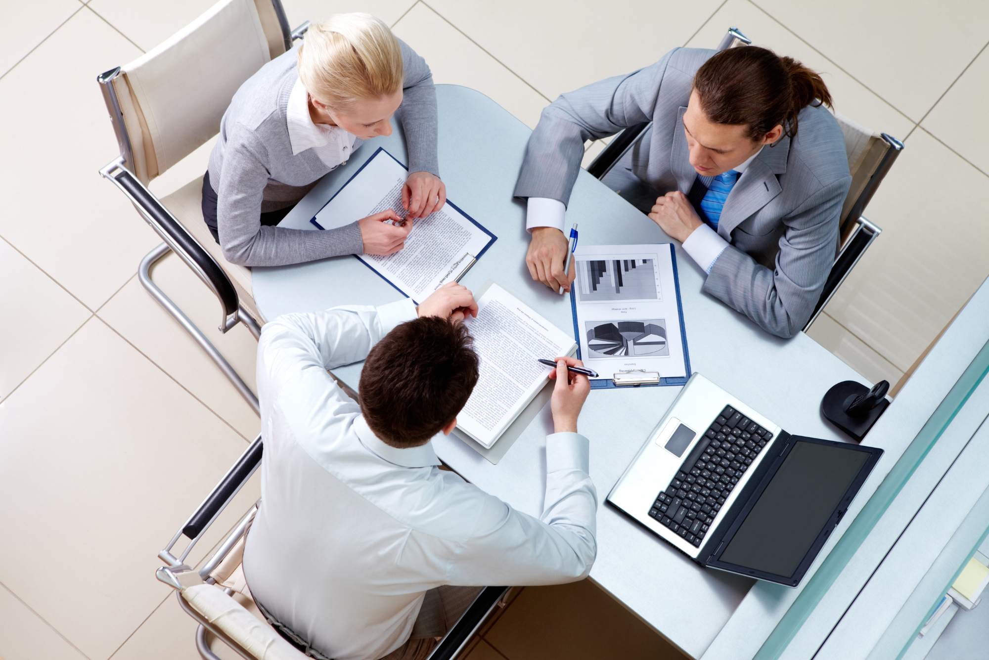 Three business professionals sitting at a table, discussing documents and charts, emphasizing analysis in sales.
