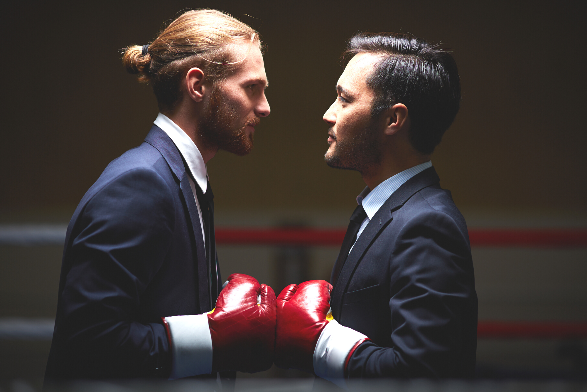 Two businessmen wearing boxing gloves stand face to face, representing competitive business.