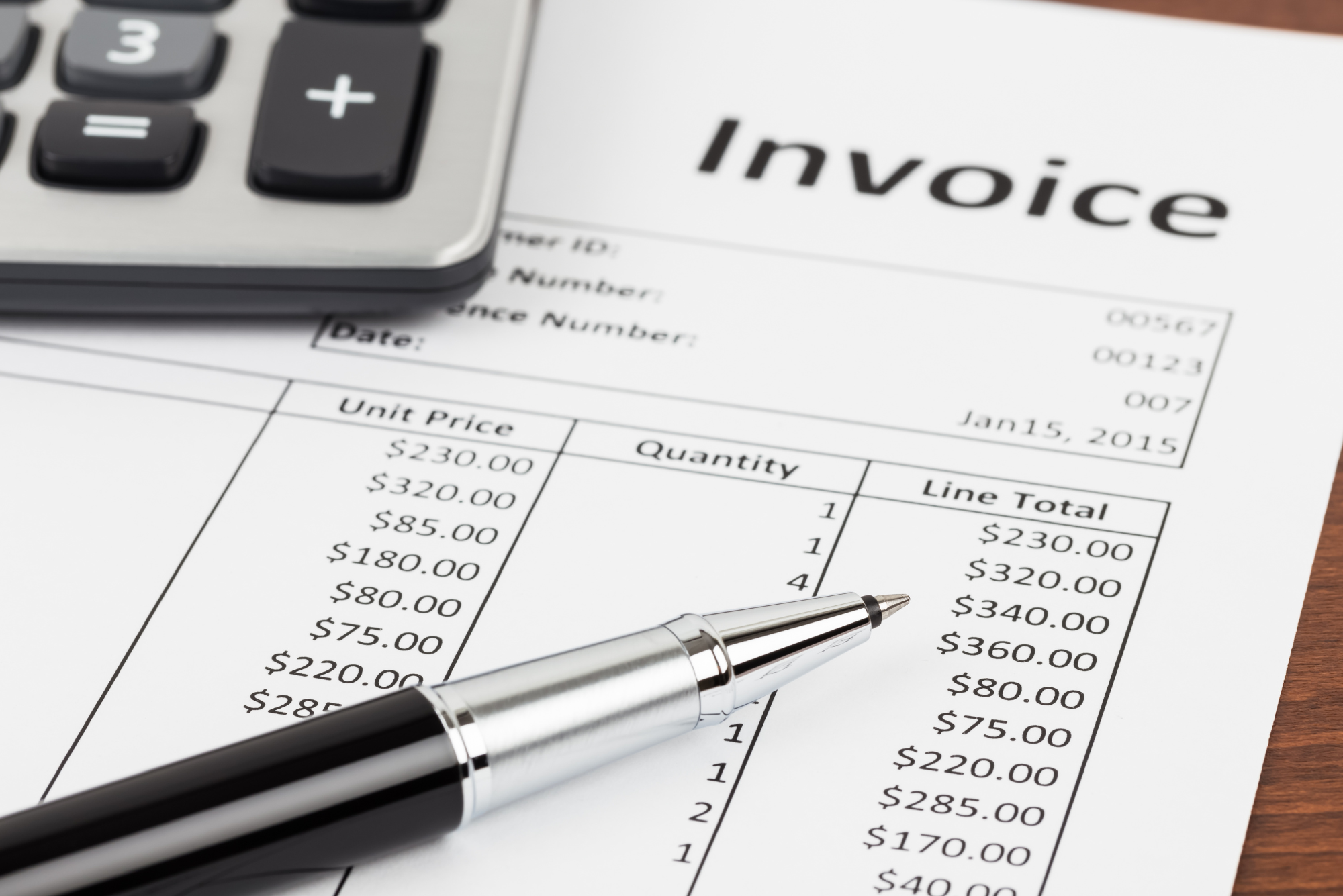 A close up of a pen, a calculator, and the line items on an invoice represents an updated pricing strategy.