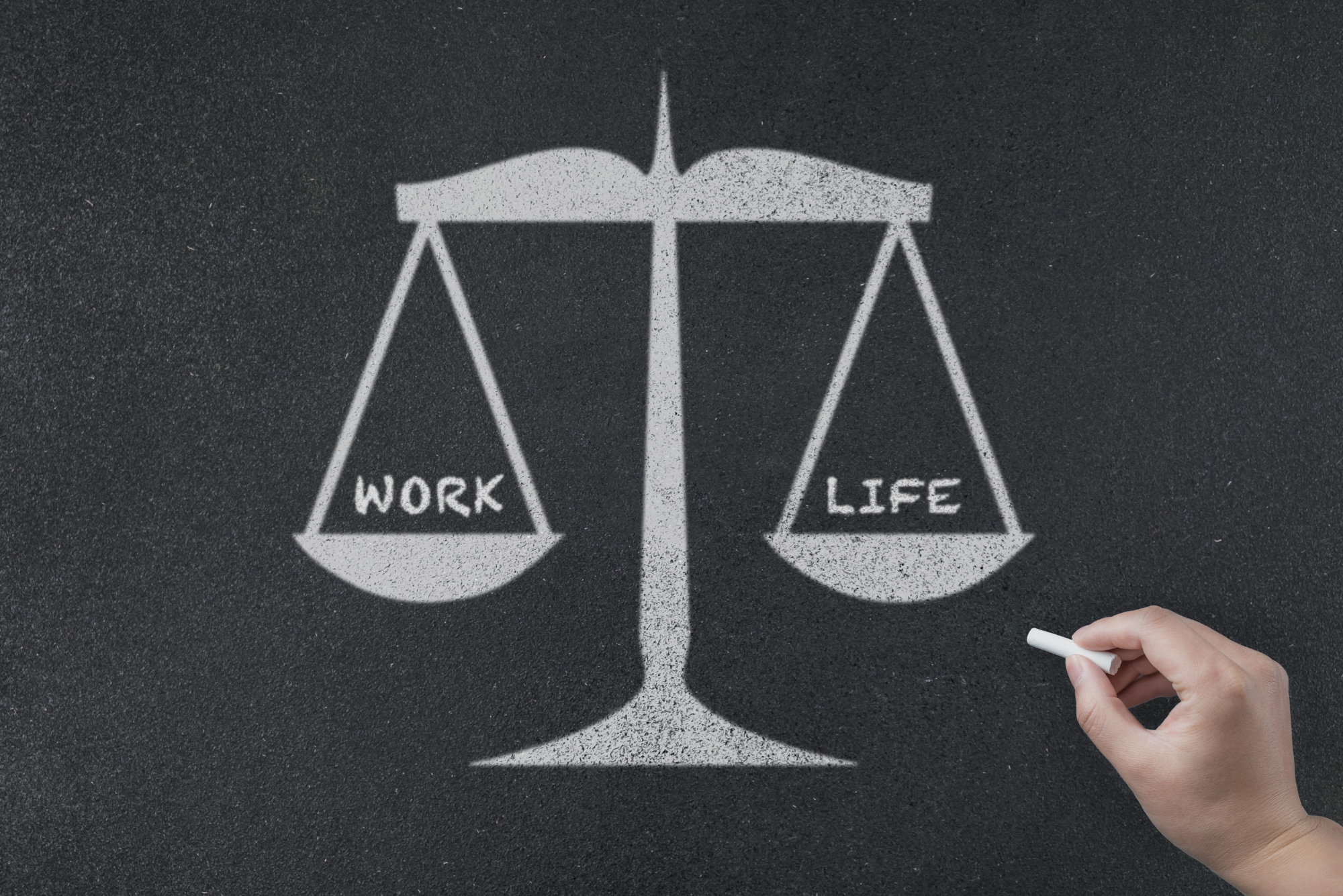 A set of scales drawn on a chalkboard holds work on one side and life on the other, representing work-life balance.