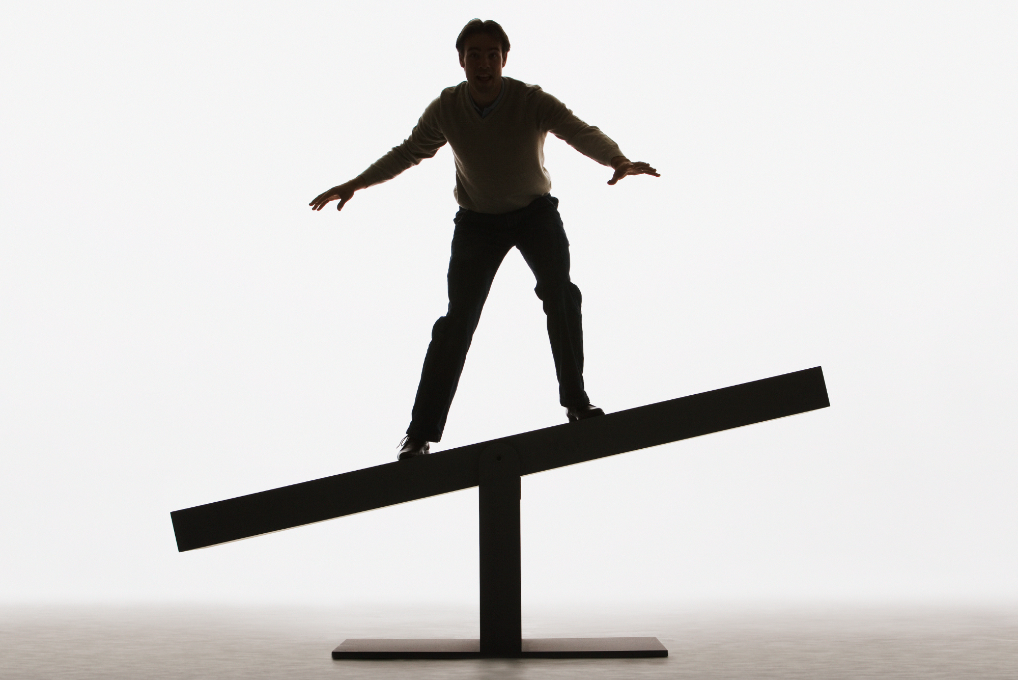 A man balances on the middle of a seesaw, representing the balance between extreme insourcing and outsourcing in scalability.