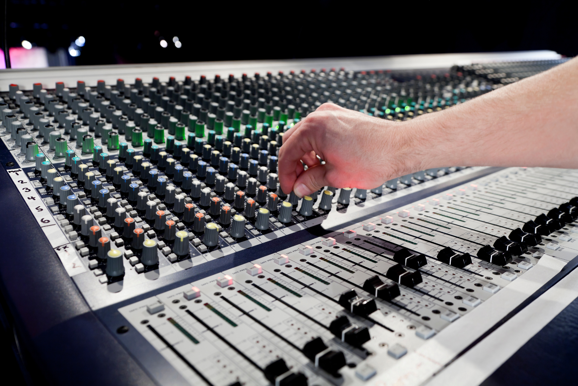 The hand of a good freelancer fiddles with a knob on a soundboard in preparation for a show.