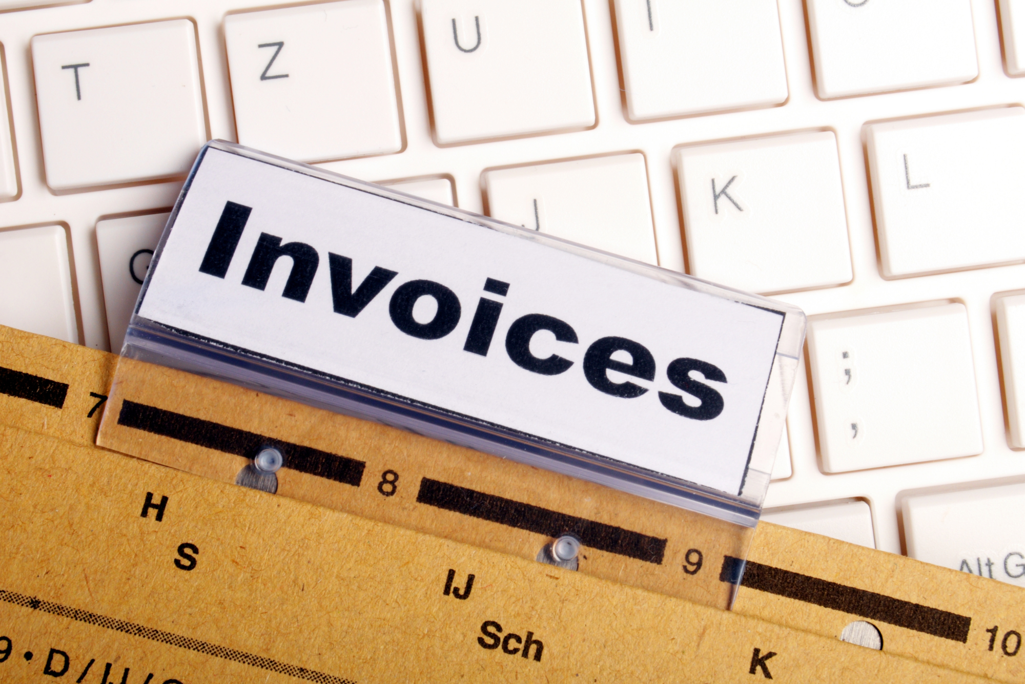 A file folder labeled “Invoices” rests on a keyboard, containing multiple invoices for a client’s recent project.