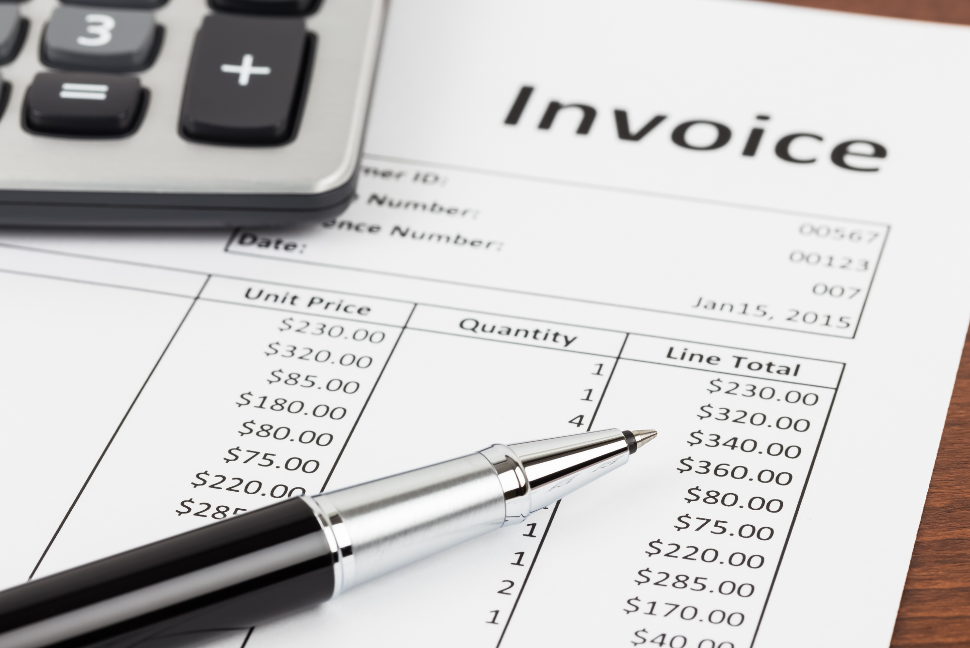 A close-up shot of an invoice shows line item pricing, with a calculator and pen resting on top.