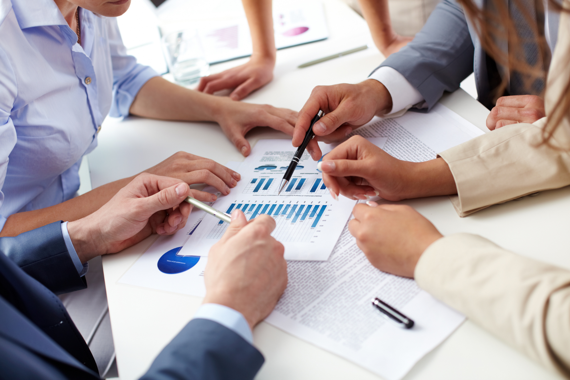 Close-up of business professionals collaborating, pointing at charts and graphs during a meeting, analyzing financial data.