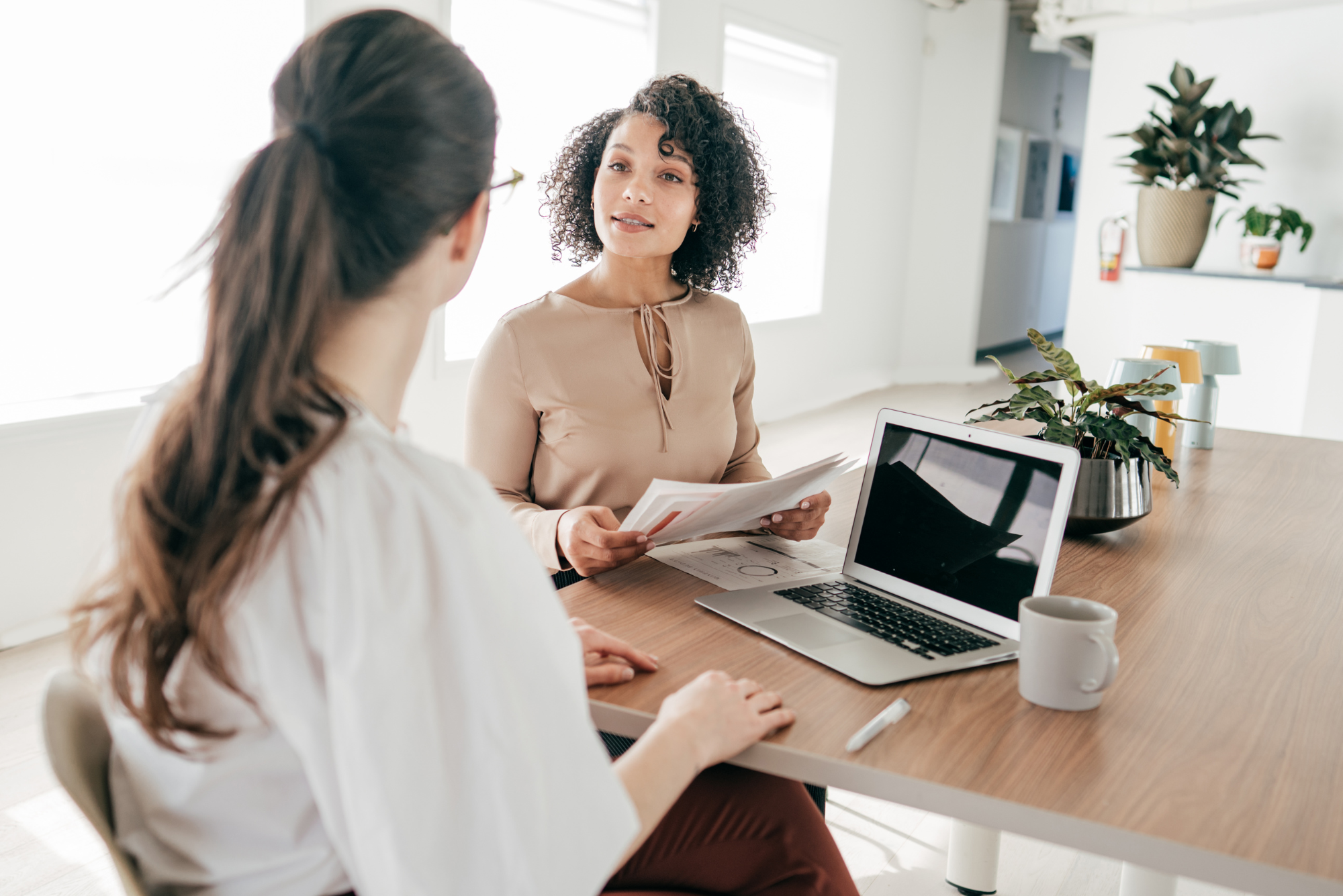 The image of two women in a discussion with documents and a laptop.