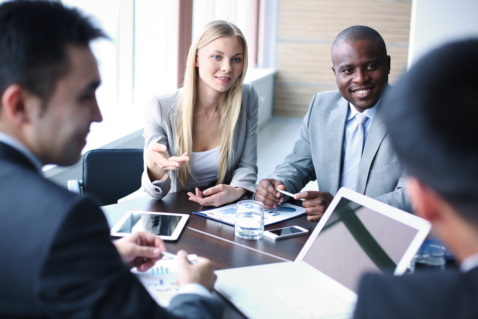 Business professionals in a meeting discussing sales strategies, with a woman explaining points to attentive colleagues.