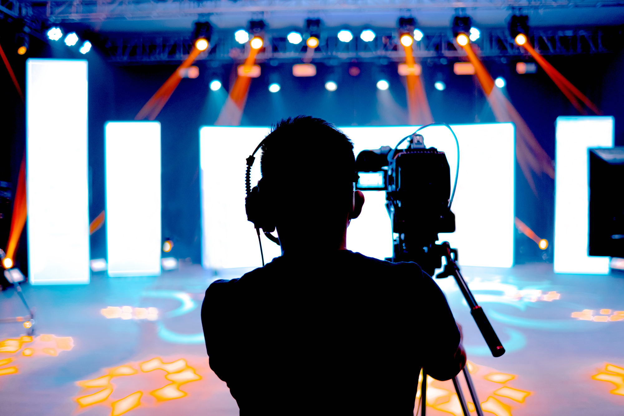 Silhouette of professional cameraman filming on well-lit stage with glowing screens.