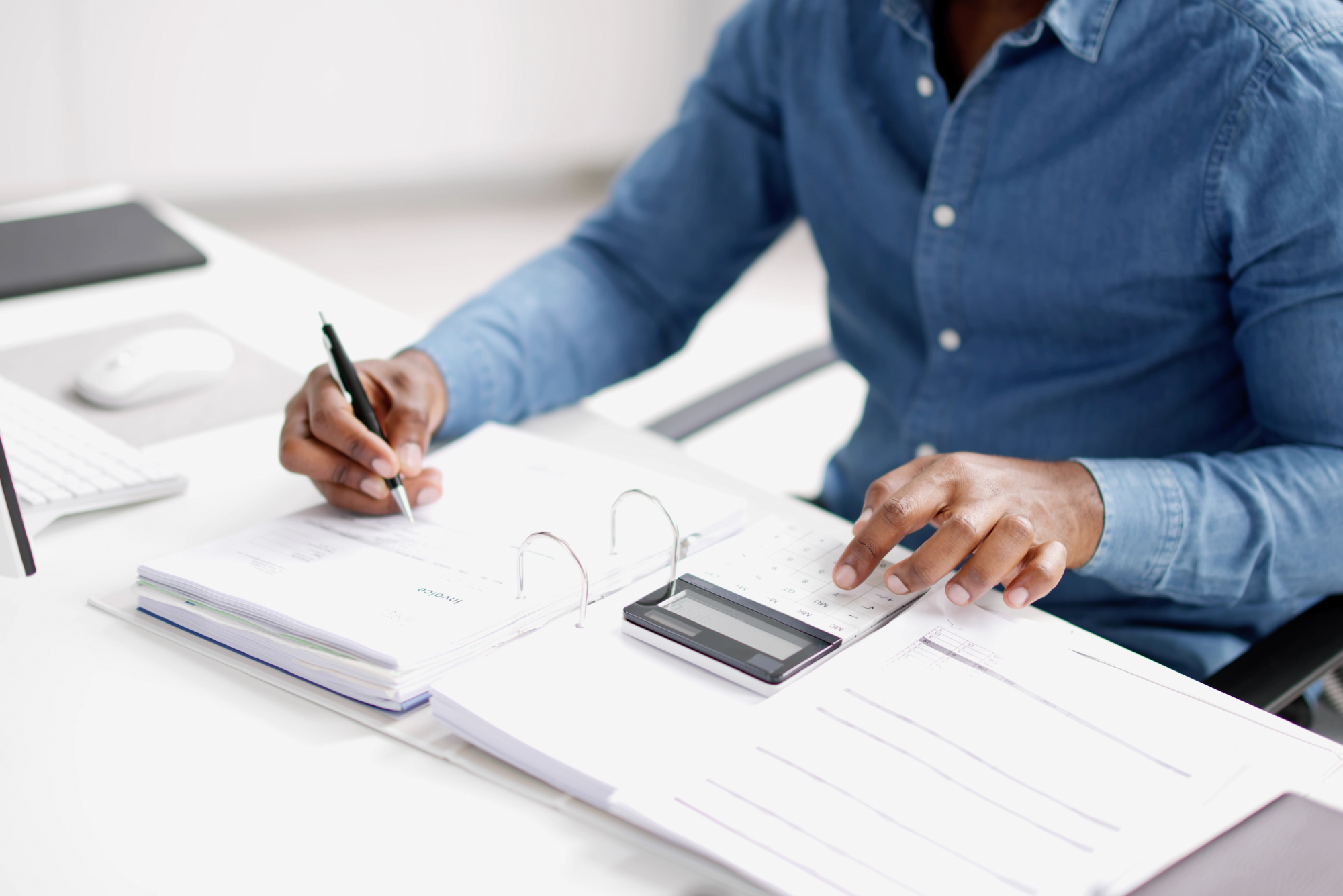 A man writing while pointing at calculator.