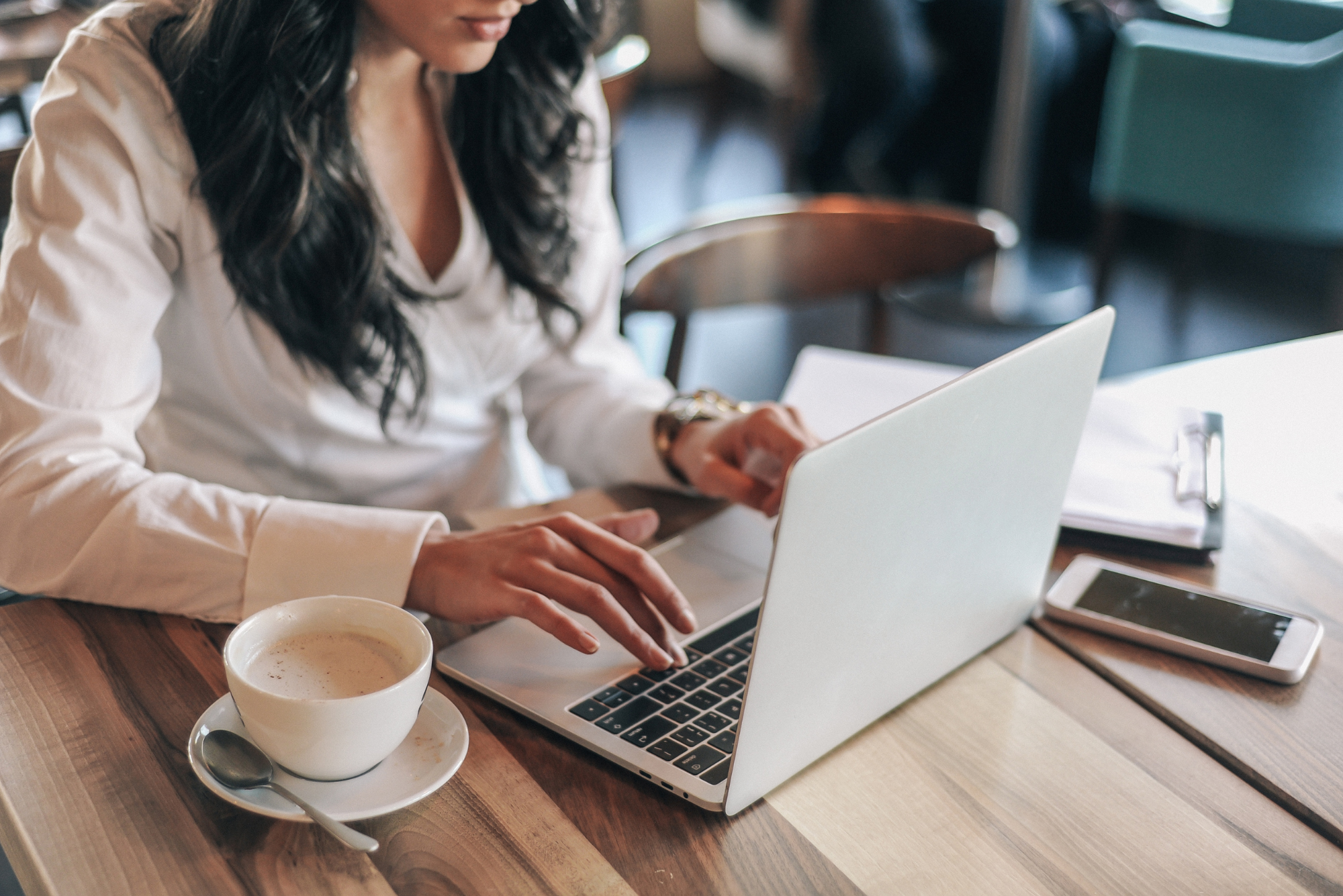 A woman working on a laptop at a wooden table.