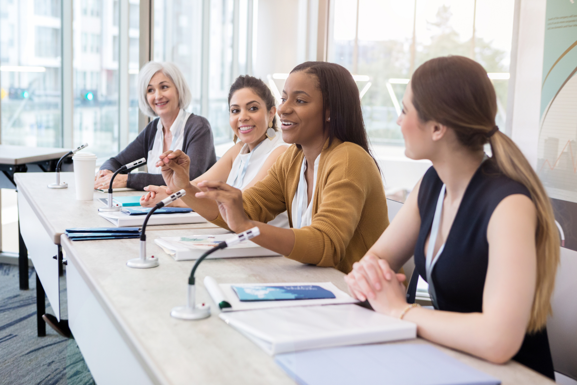 Diverse group of women speaking on a panel at a conference table.