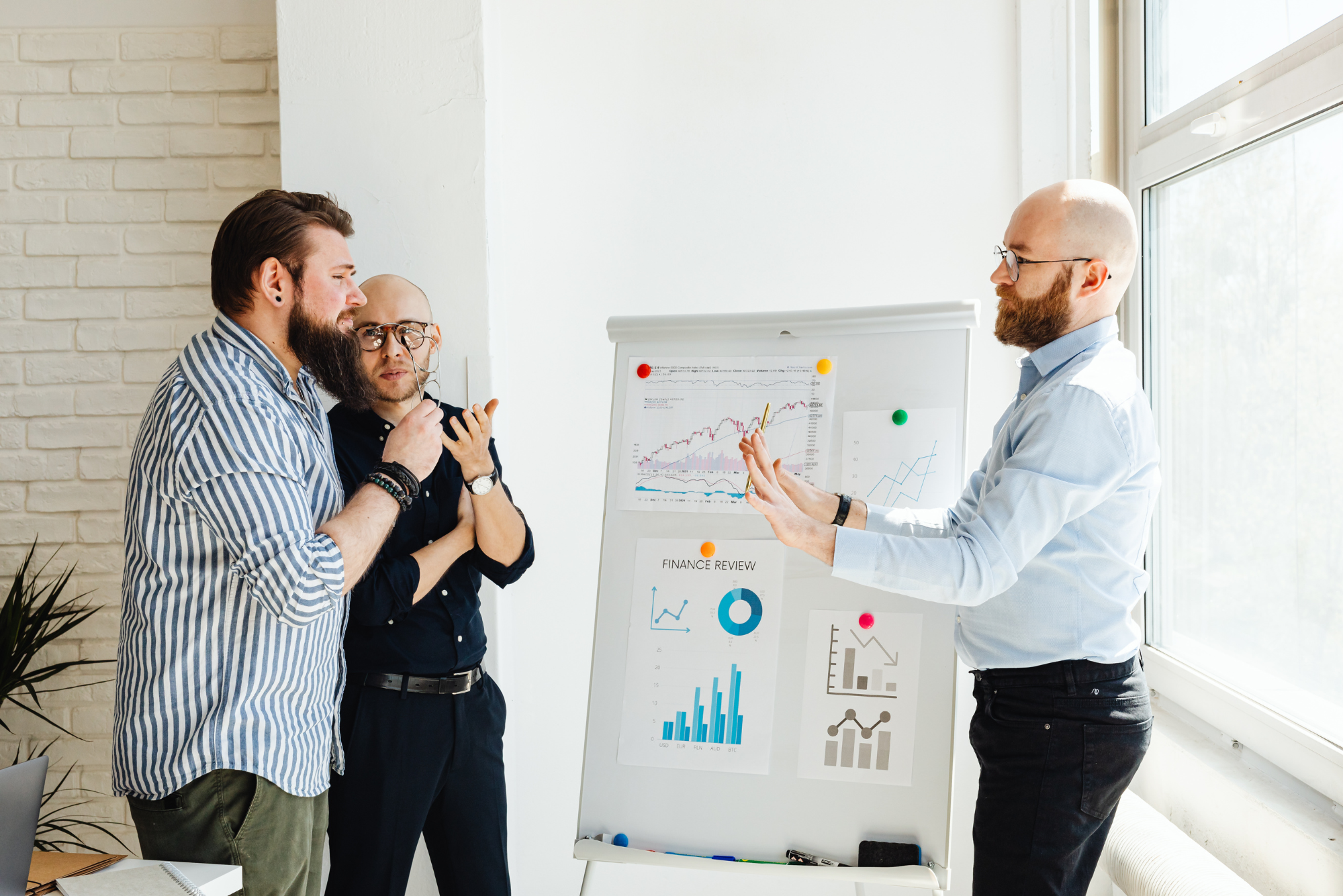 Three men discussing financial charts and trend graphs on a whiteboard.