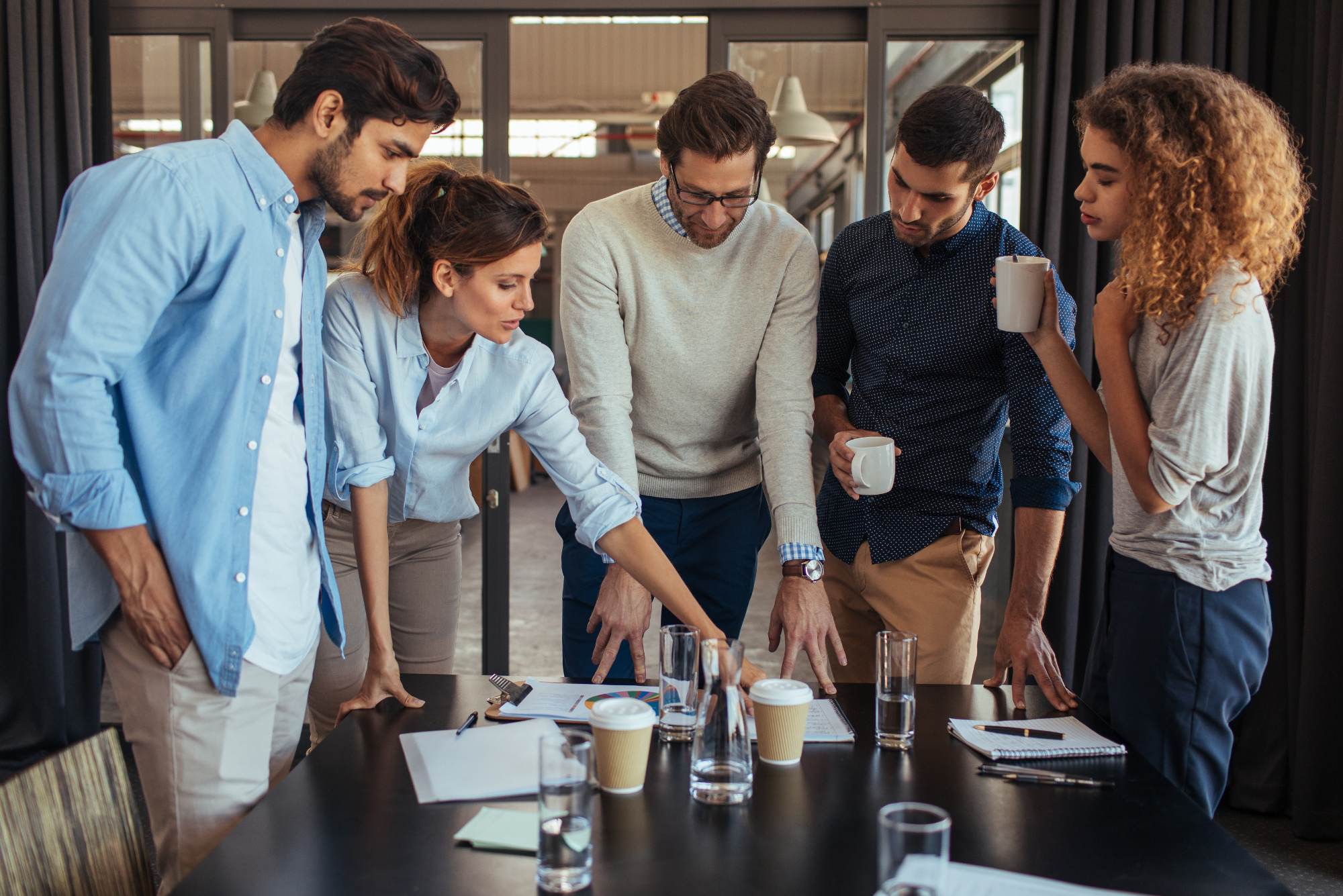 Five colleagues standing around a table reviewing documents and data together.