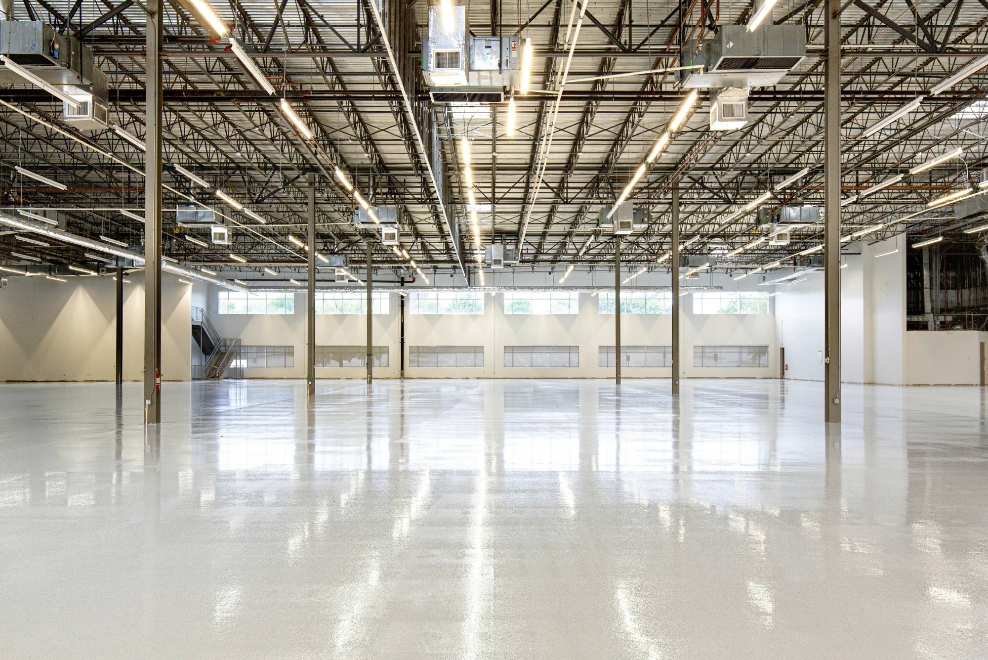 Vast empty warehouse with polished concrete floors, steel columns, and industrial lighting overhead.