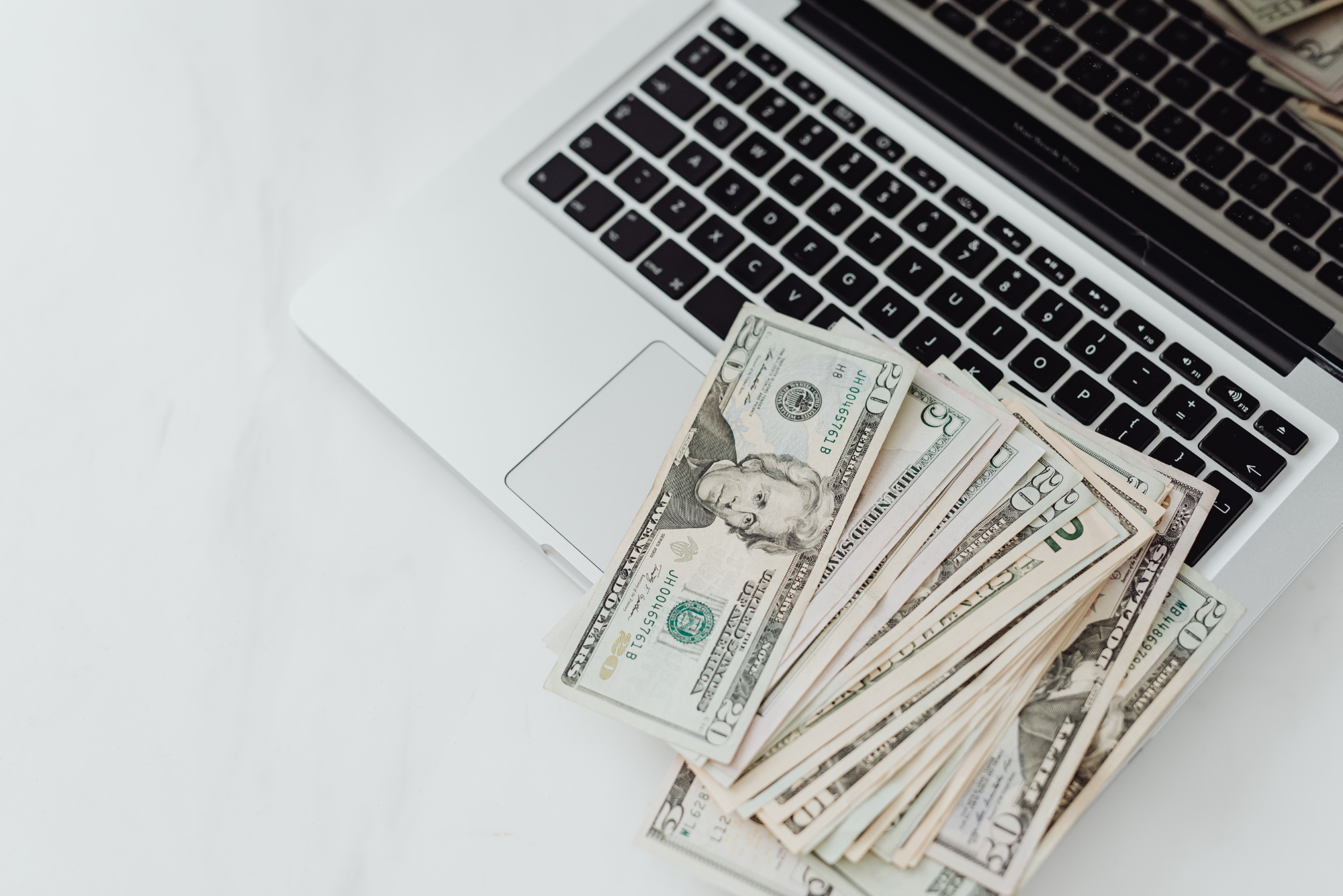 U.S. dollar bills spread across a laptop keyboard.