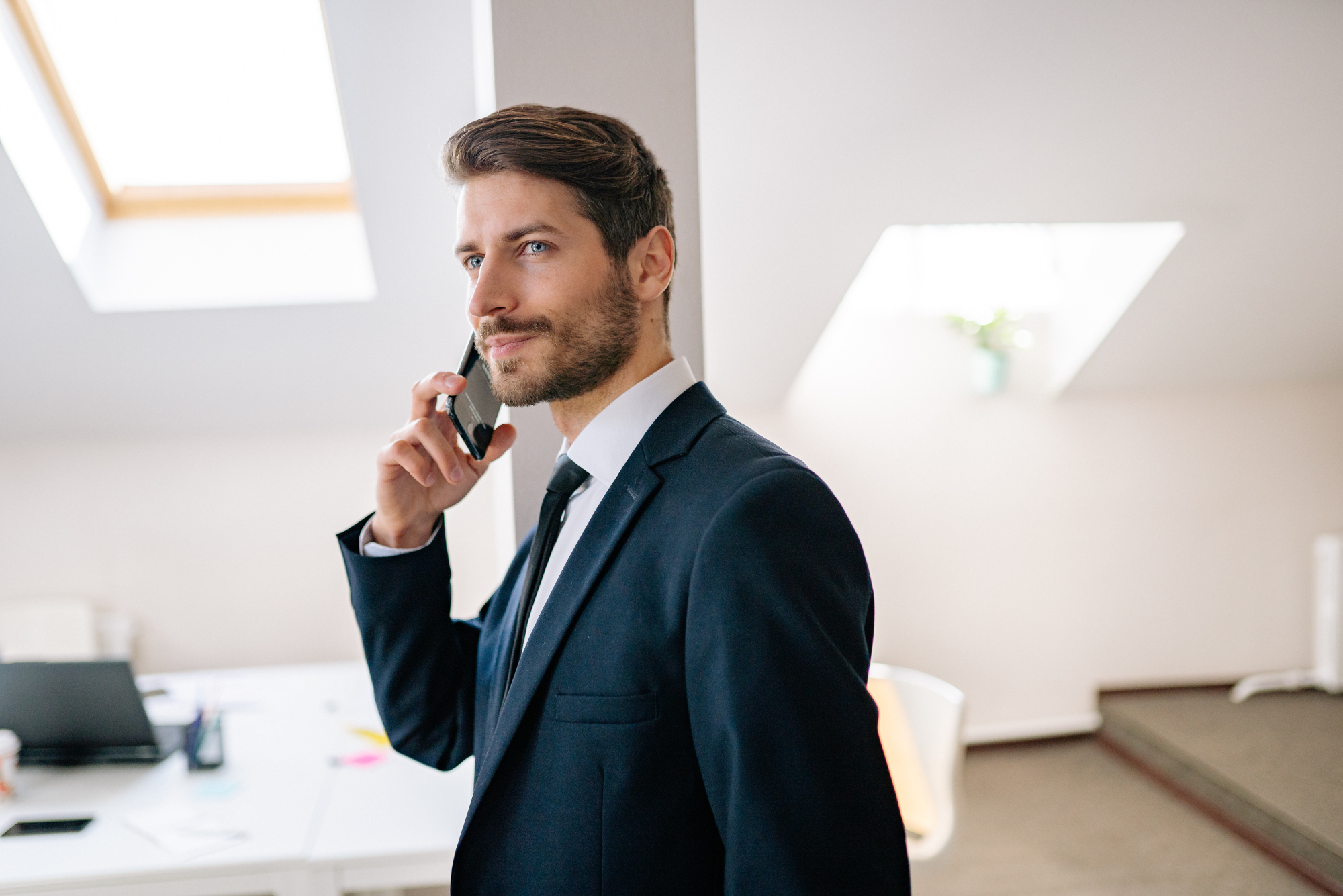 A businessman in a suit takes a phone call in a bright office.