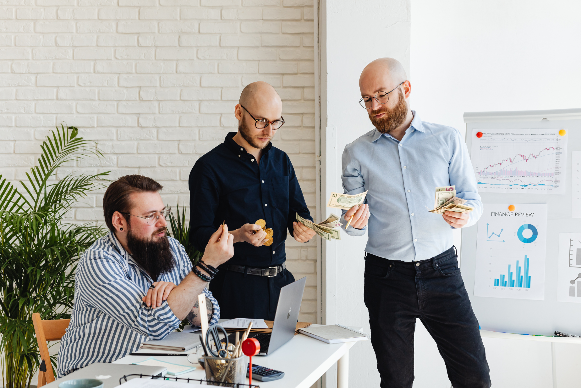 Three businessmen examine cash and coins during a finance review meeting.