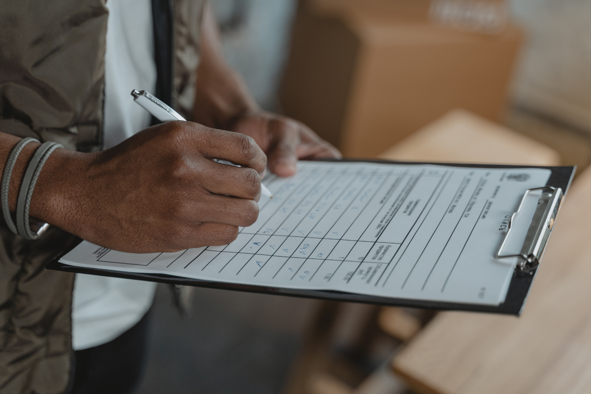 A worker fills out a checklist on a clipboard in a warehouse setting with boxes.