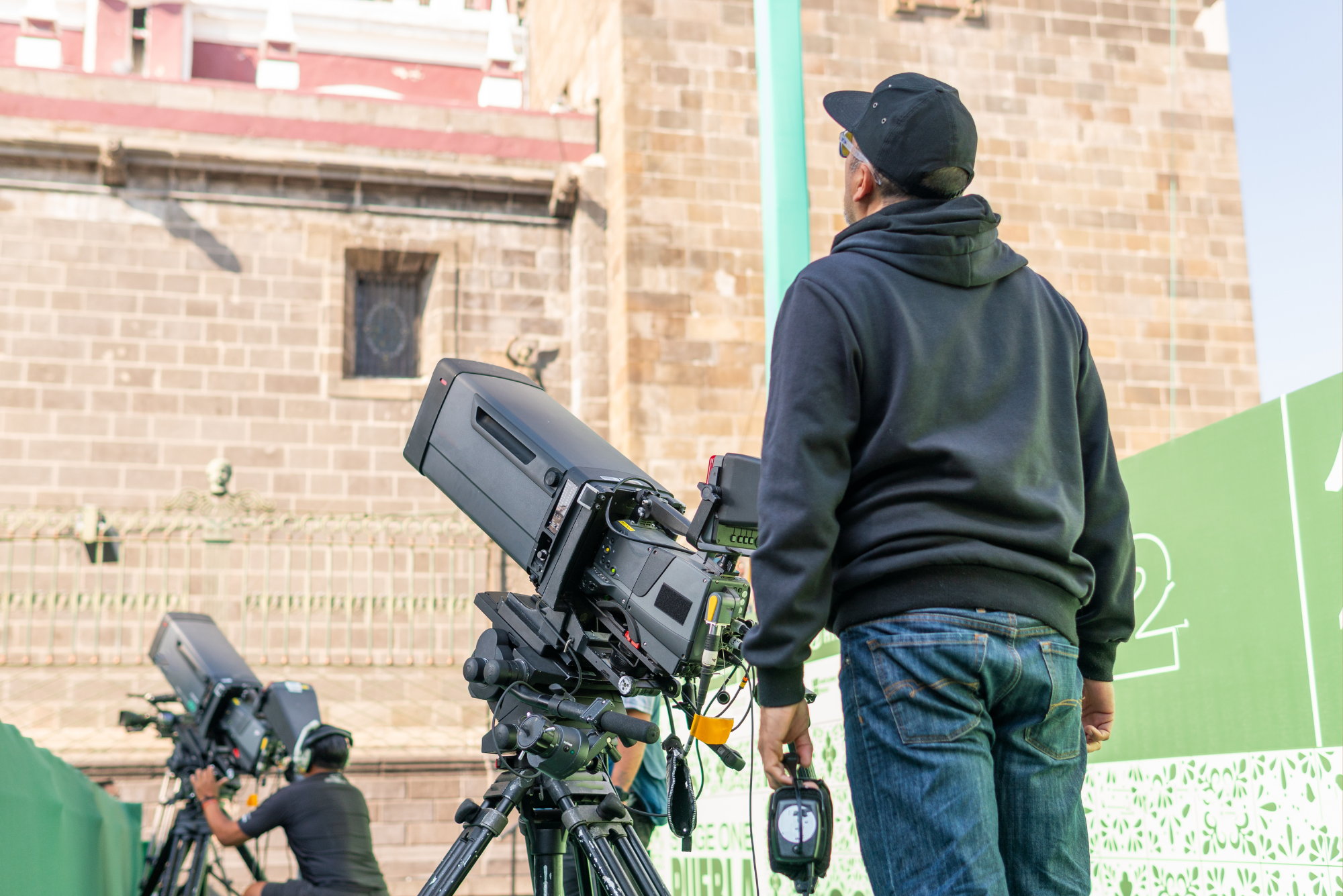 A camera operator stands beside a professional broadcast camera at an outdoor live event production setup.