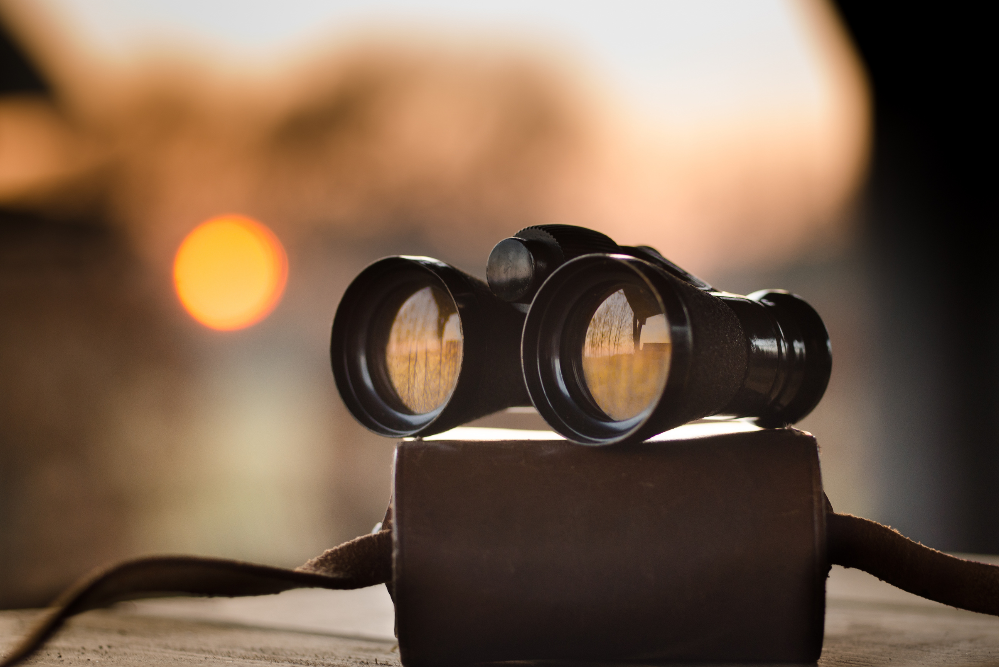 Black binoculars on a leather case at sunset, symbolizing focus and perspective; feast or famine is a choice.