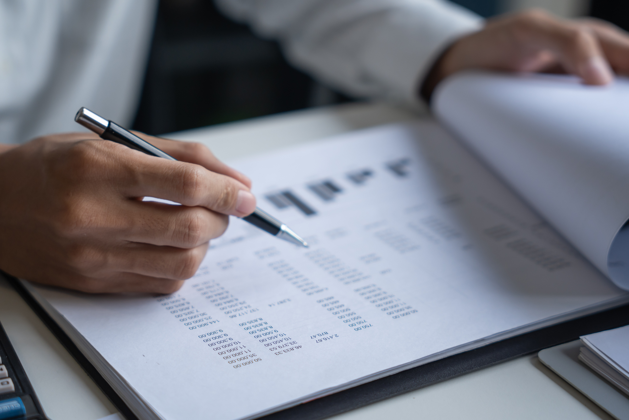 Person reviewing financial statements with a pen in hand.