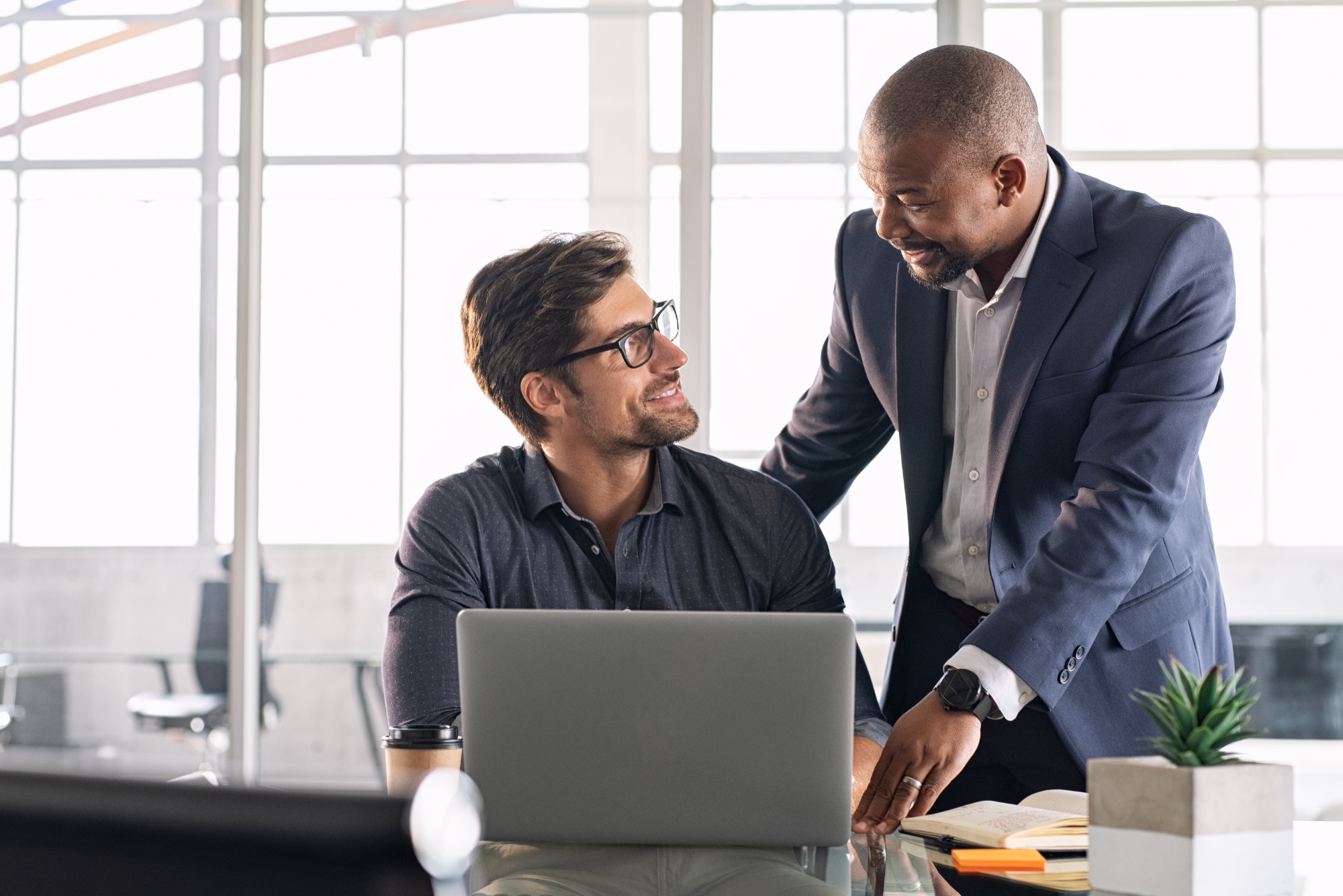 Two smiling businessmen talk over a laptop.